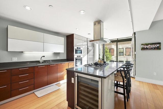 kitchen featuring island exhaust hood, appliances with stainless steel finishes, beverage cooler, white cabinets, and sink