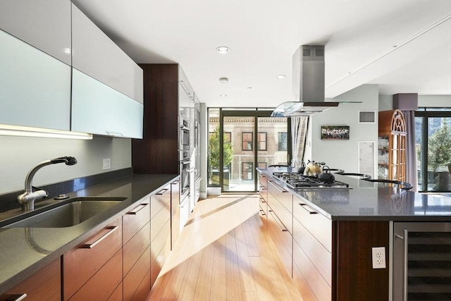 kitchen with beverage cooler, white cabinets, island exhaust hood, sink, and stainless steel gas cooktop