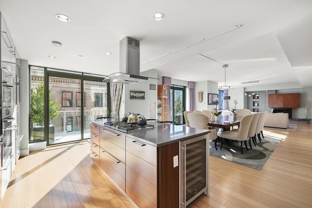 kitchen with wine cooler, light hardwood / wood-style floors, hanging light fixtures, island range hood, and stainless steel gas stovetop