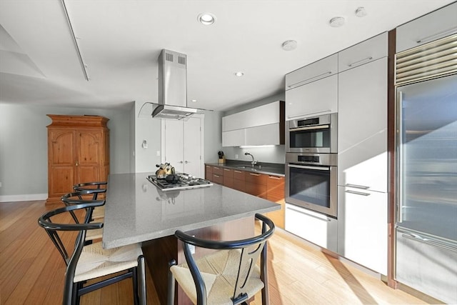 kitchen with island range hood, a breakfast bar area, stainless steel appliances, dark stone countertops, and white cabinets