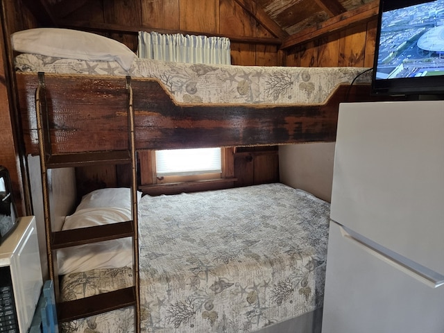 bedroom featuring lofted ceiling, wood walls, and white fridge