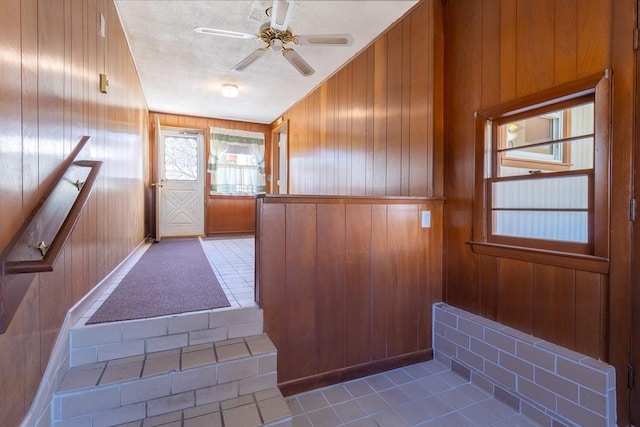 doorway to outside with tile patterned flooring, a ceiling fan, wood walls, and a textured ceiling