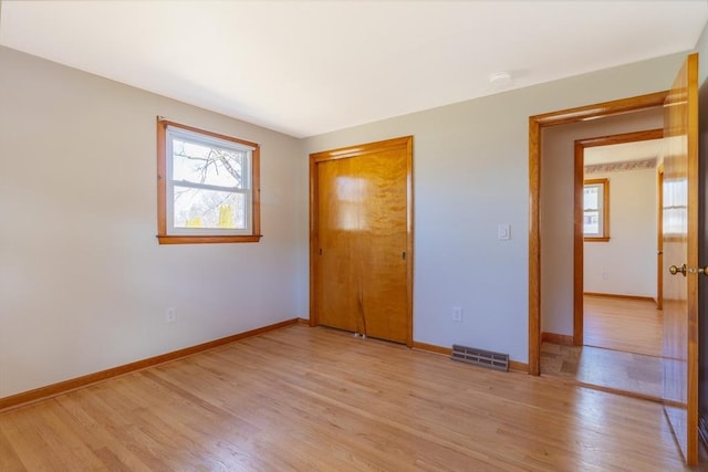 unfurnished bedroom featuring light wood-style flooring, baseboards, visible vents, and a closet