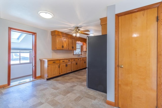 kitchen featuring baseboards, freestanding refrigerator, a sink, light countertops, and tasteful backsplash