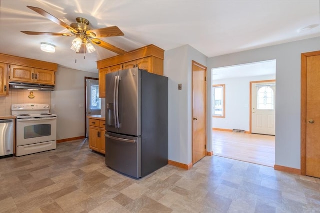 kitchen with under cabinet range hood, stainless steel appliances, light countertops, decorative backsplash, and baseboards