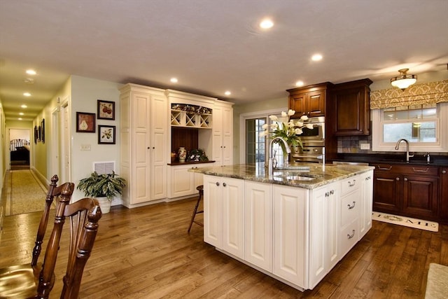 kitchen with dark wood-type flooring, sink, a breakfast bar, and a kitchen island with sink