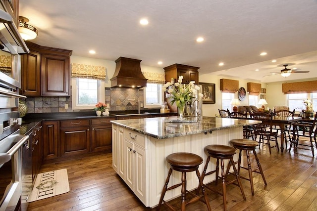 kitchen featuring a kitchen island, tasteful backsplash, premium range hood, a kitchen breakfast bar, and dark hardwood / wood-style floors