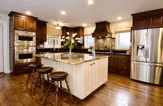 kitchen featuring premium range hood, stainless steel appliances, dark hardwood / wood-style flooring, dark stone counters, and a center island