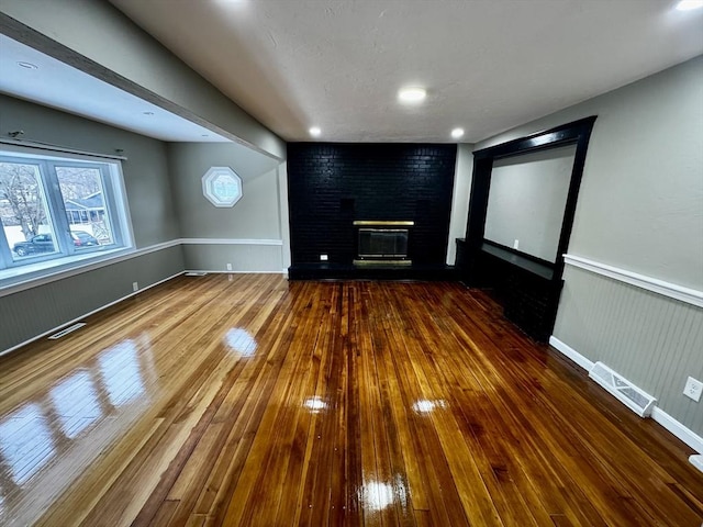 interior space featuring wainscoting, a fireplace, visible vents, and hardwood / wood-style flooring