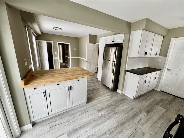 kitchen featuring tasteful backsplash, white cabinets, light wood-style flooring, butcher block countertops, and freestanding refrigerator