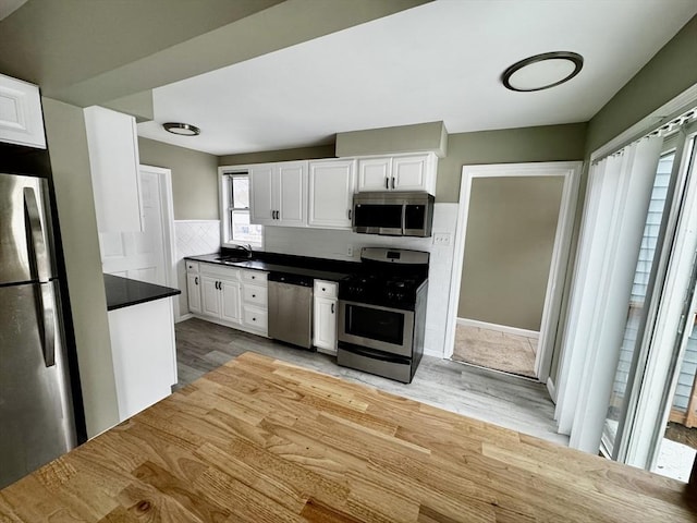 kitchen featuring stainless steel appliances, dark countertops, light wood-style flooring, white cabinets, and a sink