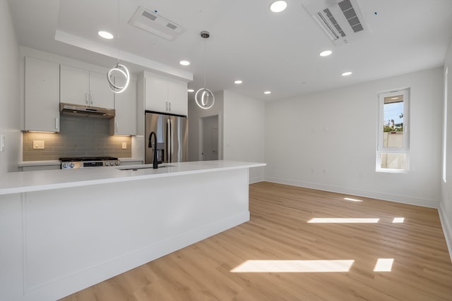 kitchen with light wood-type flooring, stainless steel appliances, sink, decorative light fixtures, and white cabinetry