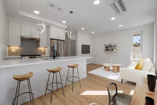 kitchen with light hardwood / wood-style flooring, backsplash, decorative light fixtures, white cabinets, and appliances with stainless steel finishes