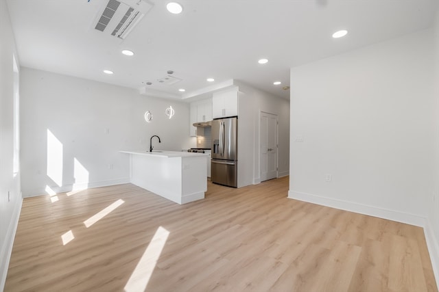 kitchen featuring stainless steel refrigerator with ice dispenser, light wood-type flooring, a breakfast bar, a kitchen island with sink, and white cabinets