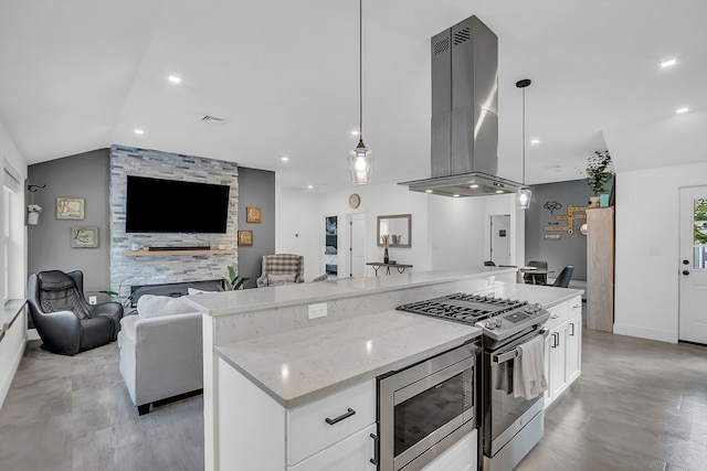 kitchen featuring appliances with stainless steel finishes, island range hood, white cabinetry, and a stone fireplace