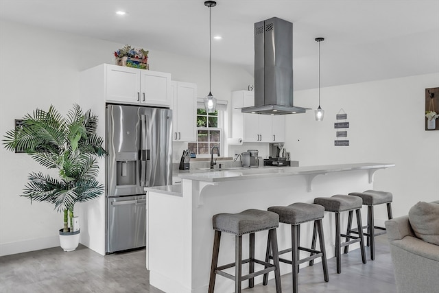 kitchen with white cabinets, hanging light fixtures, stainless steel fridge, island exhaust hood, and a breakfast bar