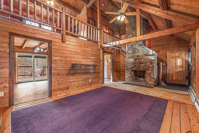 unfurnished living room with a fireplace, beam ceiling, wooden ceiling, and wood walls