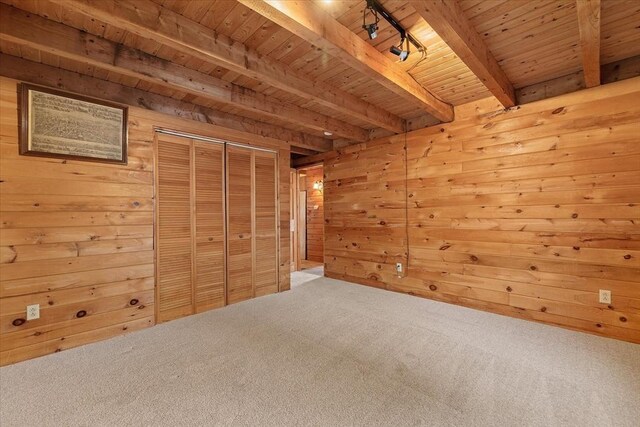 interior space with beamed ceiling, carpet, track lighting, and wooden walls