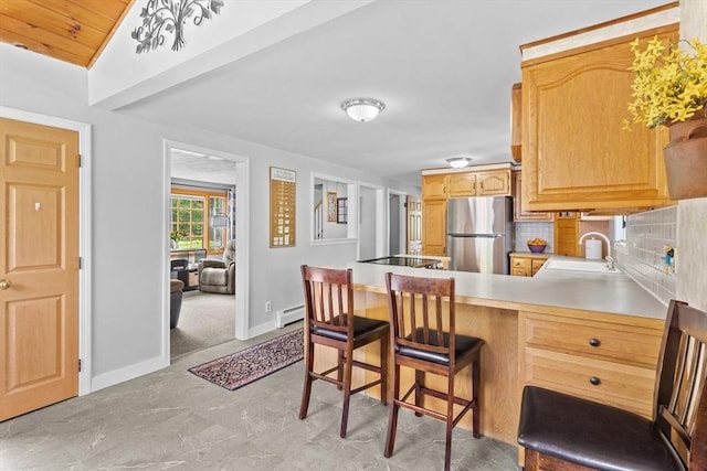 kitchen featuring freestanding refrigerator, a baseboard heating unit, a sink, a peninsula, and baseboards