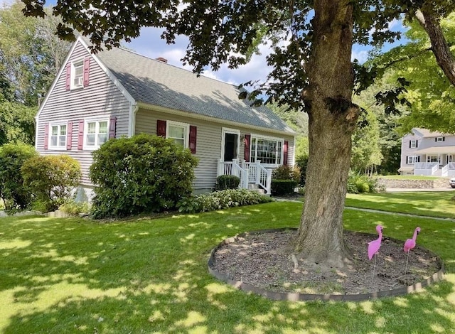 view of front facade with a front yard and a shingled roof