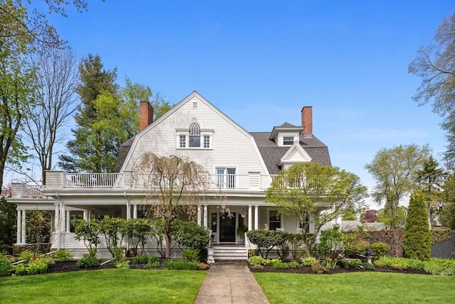 shingle-style home with a balcony, a chimney, a gambrel roof, and a porch