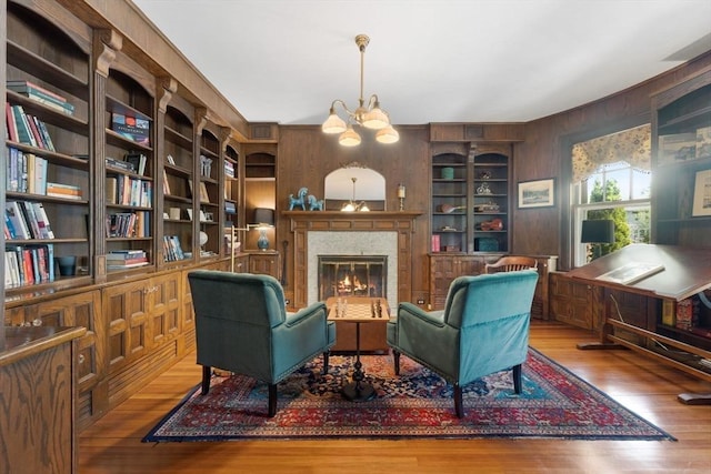 sitting room with wooden walls, built in shelves, wood finished floors, a glass covered fireplace, and a chandelier