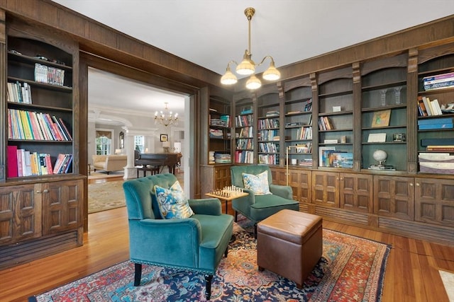 living area with a chandelier, crown molding, wood finished floors, arched walkways, and built in shelves
