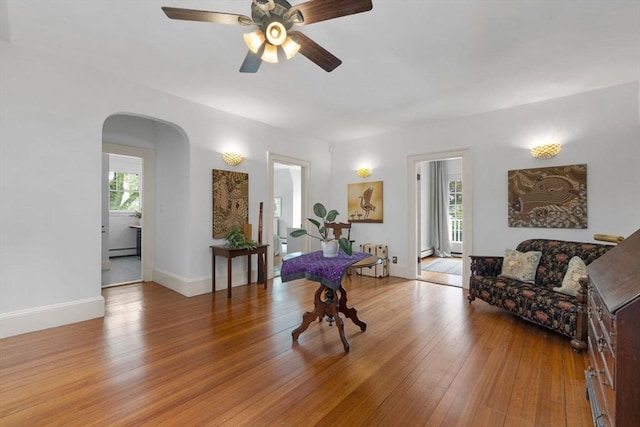 playroom featuring healthy amount of natural light, arched walkways, baseboard heating, and wood finished floors