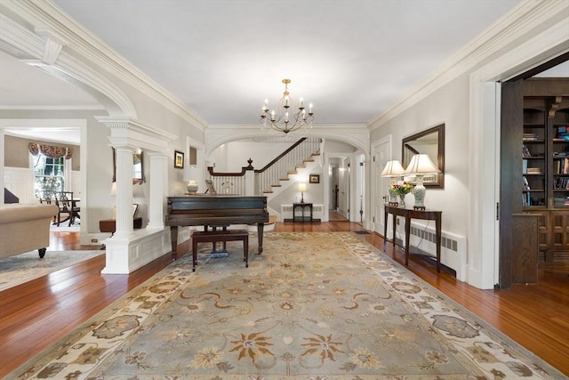 foyer entrance featuring radiator, wood finished floors, crown molding, stairs, and decorative columns