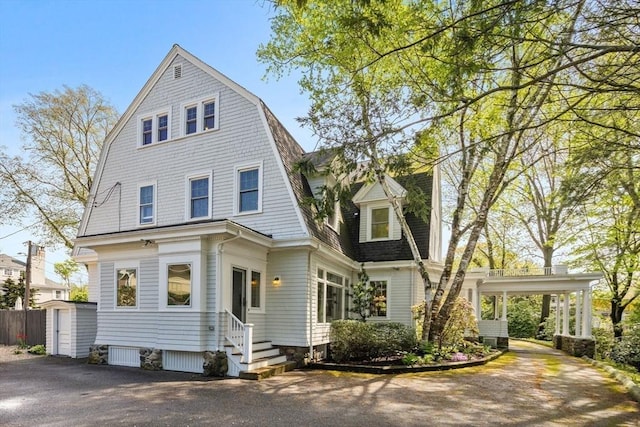 colonial inspired home with entry steps, a storage shed, a gambrel roof, driveway, and an outbuilding