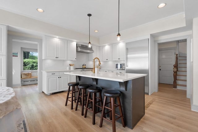 kitchen with under cabinet range hood, light countertops, white cabinetry, light wood-style floors, and recessed lighting