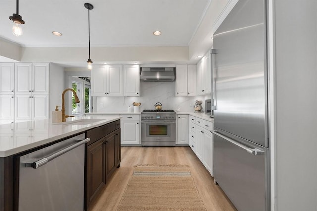 kitchen featuring high end appliances, a sink, ventilation hood, white cabinets, and ornamental molding