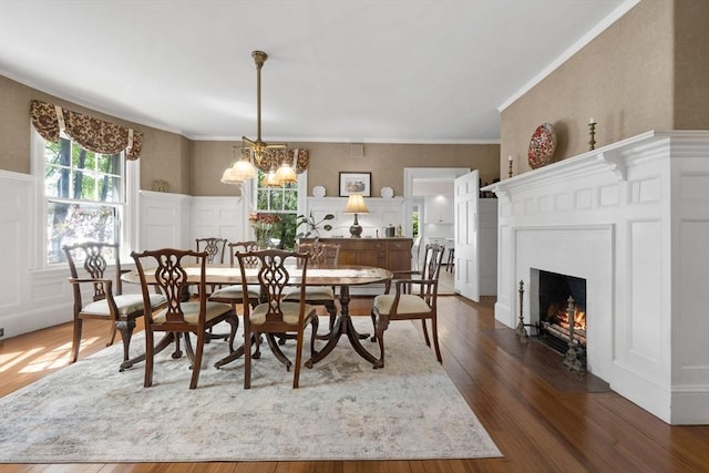 dining room with a decorative wall, dark wood-type flooring, a lit fireplace, a wainscoted wall, and a chandelier
