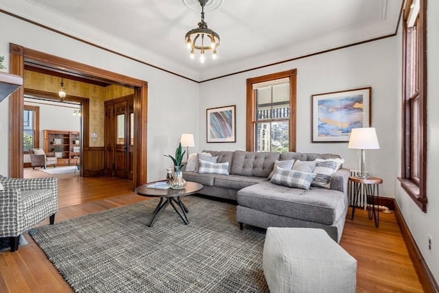 living room with wood finished floors, baseboards, a wainscoted wall, crown molding, and a chandelier