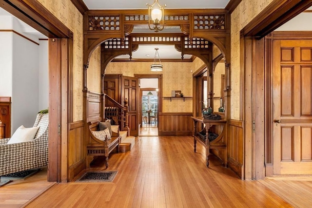 entryway with a wainscoted wall, ornamental molding, arched walkways, light wood finished floors, and stairs