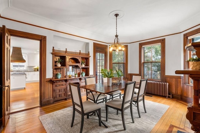 dining room with radiator heating unit, ornamental molding, wainscoting, light wood-type flooring, and a chandelier