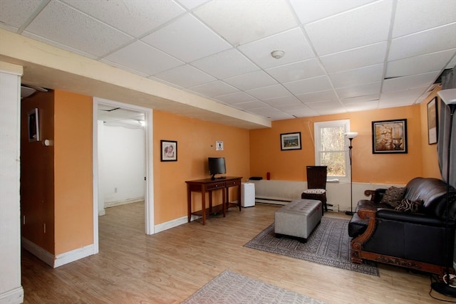 living room with a drop ceiling, light hardwood / wood-style floors, and a baseboard radiator