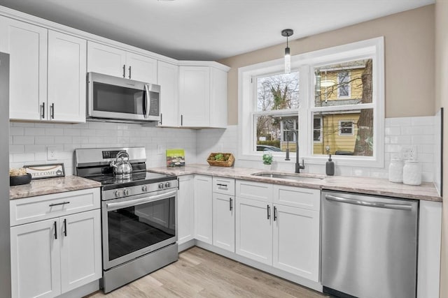 kitchen featuring white cabinetry, sink, stainless steel appliances, light stone counters, and pendant lighting