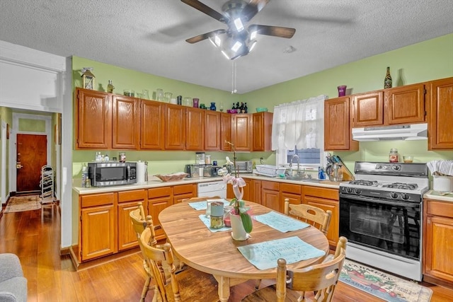 kitchen with range with gas stovetop, light wood finished floors, light countertops, under cabinet range hood, and stainless steel microwave