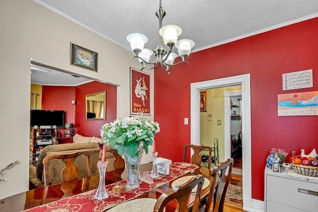 dining space featuring a notable chandelier, ornamental molding, a textured ceiling, wood finished floors, and baseboards