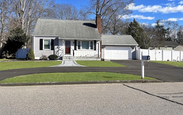 colonial inspired home with a front yard, fence, a chimney, a garage, and aphalt driveway