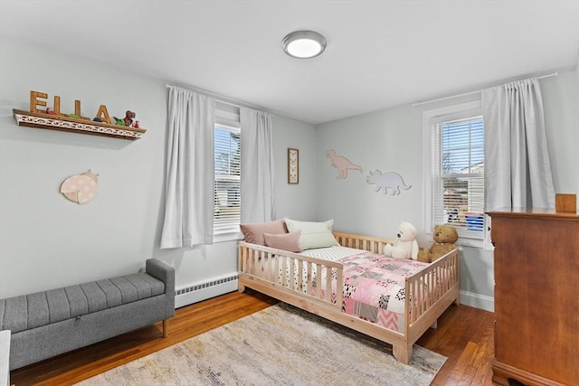 bedroom featuring a baseboard heating unit, wood finished floors, and baseboards