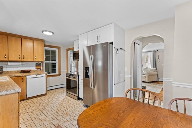 kitchen with arched walkways, stainless steel appliances, light countertops, a baseboard heating unit, and backsplash