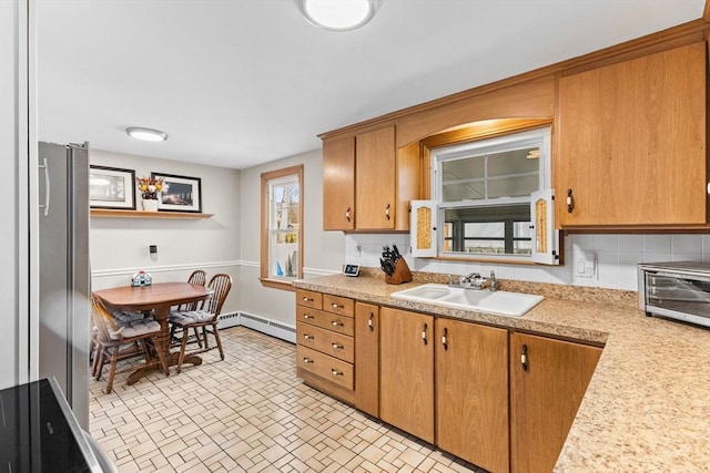 kitchen featuring backsplash, a baseboard heating unit, light countertops, brown cabinetry, and a sink