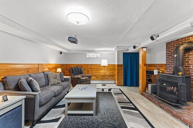 living room featuring a wainscoted wall, a textured ceiling, a wood stove, and light wood-type flooring