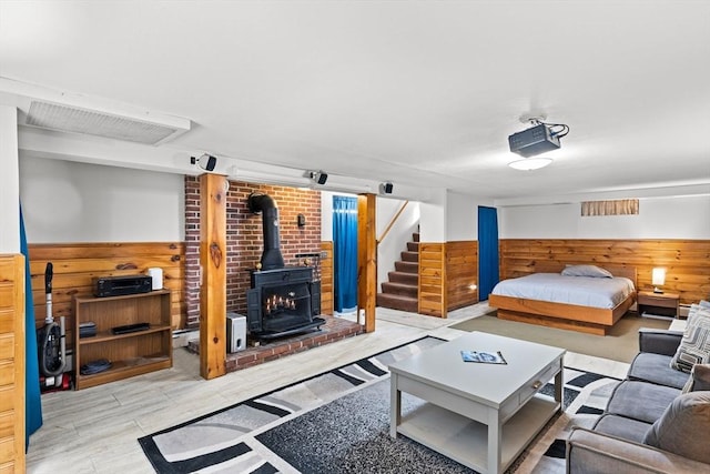 bedroom featuring a wood stove, wood finished floors, wood walls, and wainscoting