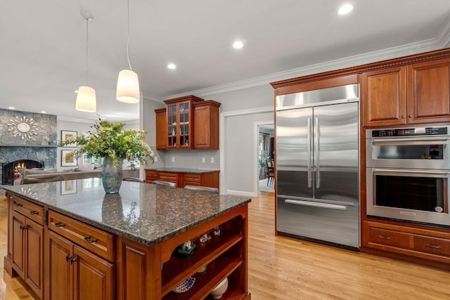 127 Shade St, Lexington, MA 02421 - kitchen featuring stainless steel appliances, brown cabinetry, light wood-style flooring, ornamental molding, and a stone fireplace
