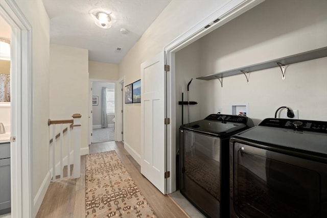 clothes washing area with washing machine and dryer and light hardwood / wood-style flooring