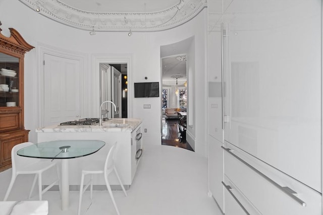 kitchen featuring a kitchen island with sink, light stone countertops, stainless steel gas cooktop, and a sink