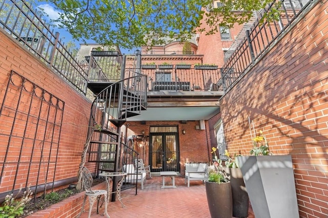 back of house with stairs, brick siding, a patio area, a balcony, and french doors